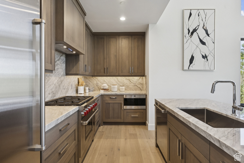 Kitchen featuring high quality appliances, light wood-style flooring, decorative backsplash, light stone counters, and recessed lighting