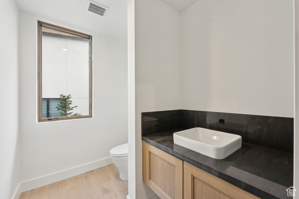 Half bath with wood finished floors, toilet, baseboards, and vanity