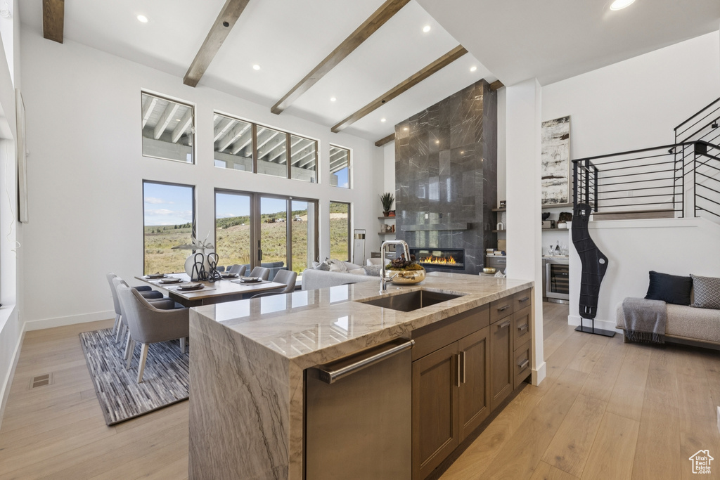 Kitchen featuring open floor plan, a large fireplace, light stone counters, dishwasher, and beamed ceiling