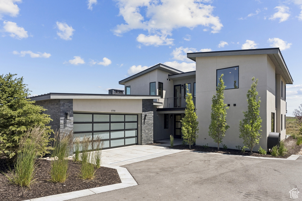 Contemporary home with stone siding, a balcony, concrete driveway, and stucco siding