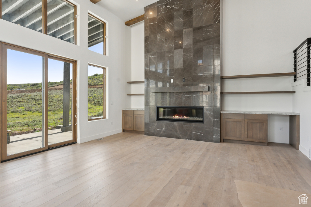 Unfurnished living room with a high end fireplace, wood finished floors, a towering ceiling, and baseboards