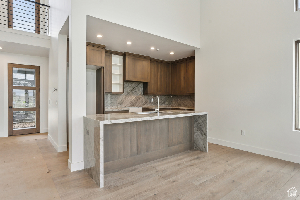 Kitchen with baseboards, a sink, tasteful backsplash, a high ceiling, and light wood-type flooring
