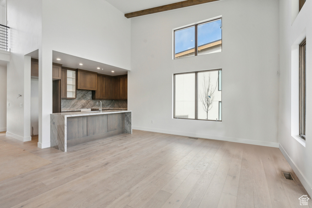 Unfurnished living room featuring a towering ceiling, baseboards, healthy amount of natural light, light wood-type flooring, and beamed ceiling