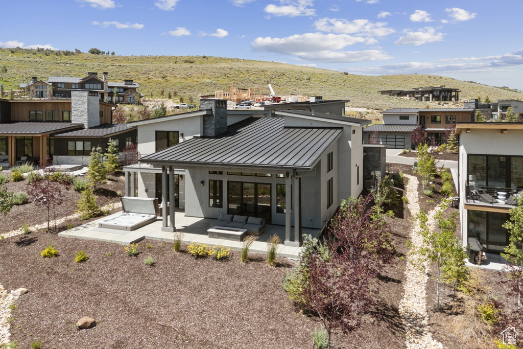 Rear view of property featuring a standing seam roof, a metal roof, a patio, a mountain view, and a chimney