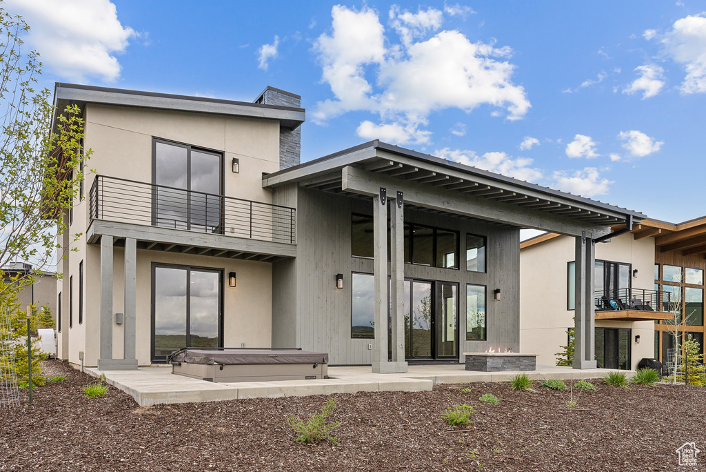 Back of house with a covered hot tub, a balcony, stucco siding, and a patio area