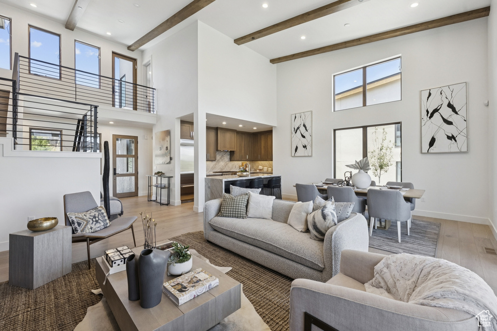 Living area featuring light wood-type flooring, a towering ceiling, recessed lighting, beamed ceiling, and stairway