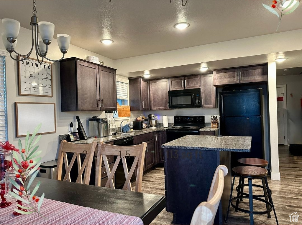 Kitchen featuring black appliances, light wood-type flooring, decorative light fixtures, light stone counters, and a chandelier