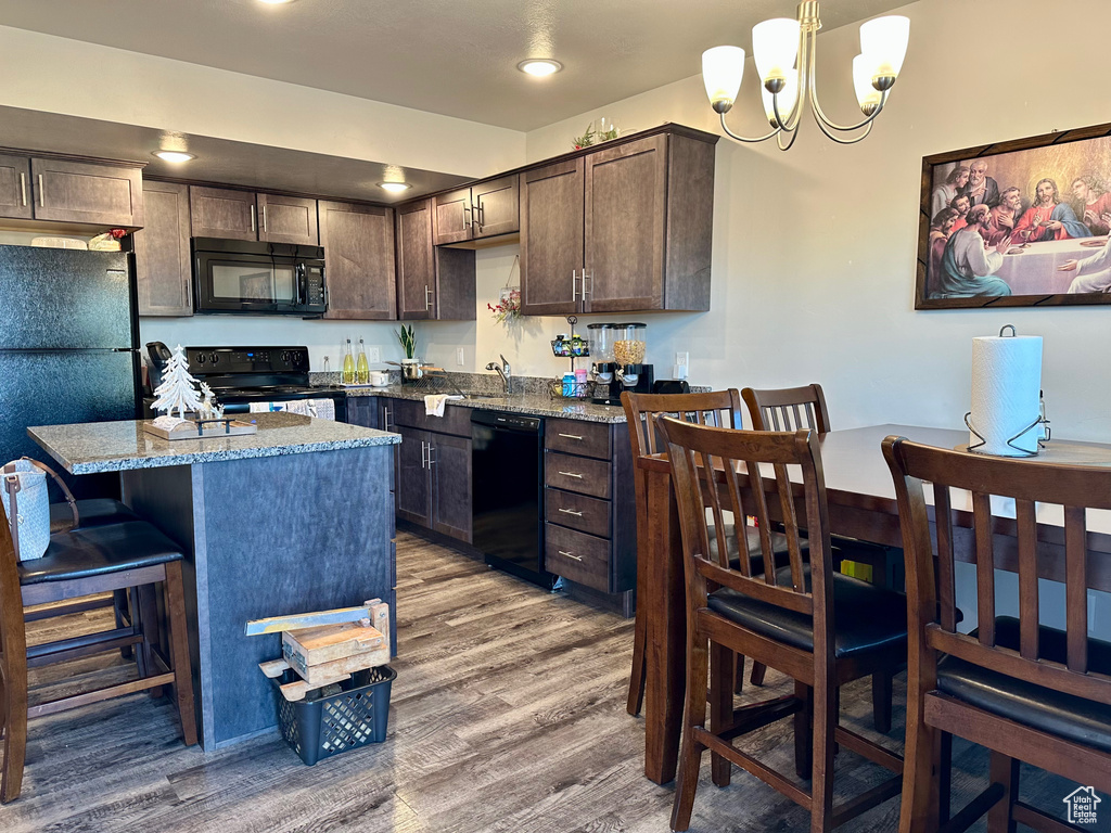 Kitchen featuring light stone counters, dark brown cabinets, black appliances, hardwood / wood-style flooring, and hanging light fixtures