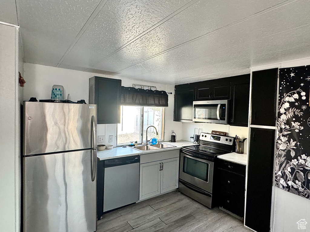 Kitchen with appliances with stainless steel finishes, a textured ceiling, light hardwood / wood-style flooring, and sink