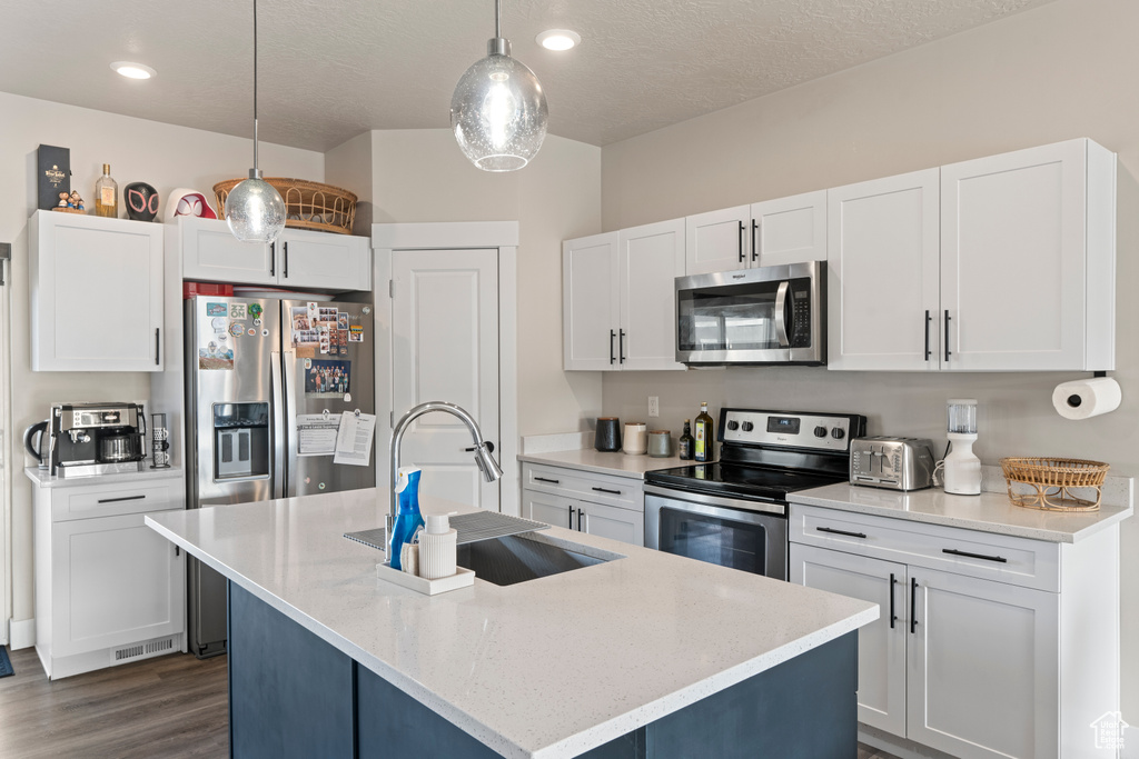 Kitchen featuring a center island with sink, sink, hanging light fixtures, dark hardwood / wood-style flooring, and stainless steel appliances