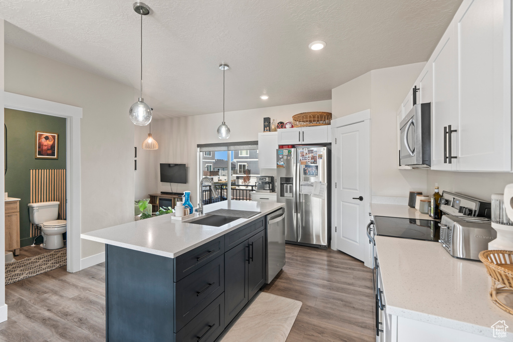 Kitchen featuring stainless steel appliances, a kitchen island with sink, decorative light fixtures, light hardwood / wood-style floors, and white cabinetry