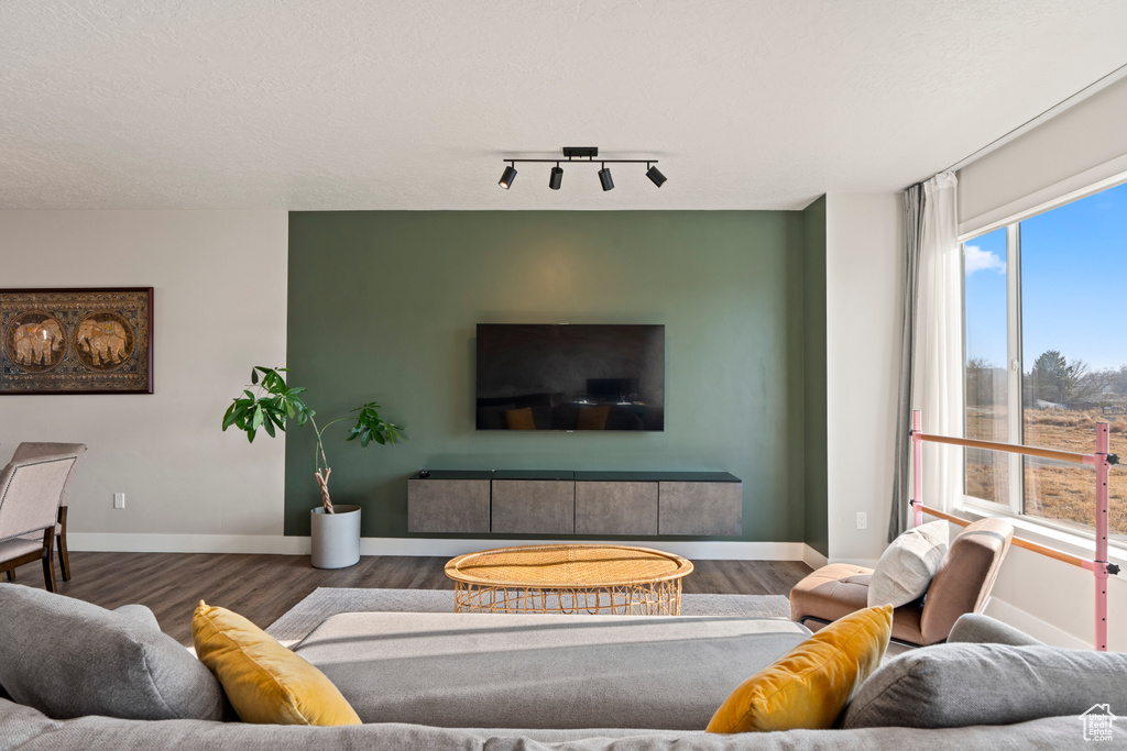 Living room with a textured ceiling, track lighting, and dark wood-type flooring