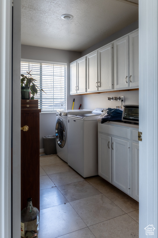 Washroom with cabinets, separate washer and dryer, a textured ceiling, and light tile patterned floors