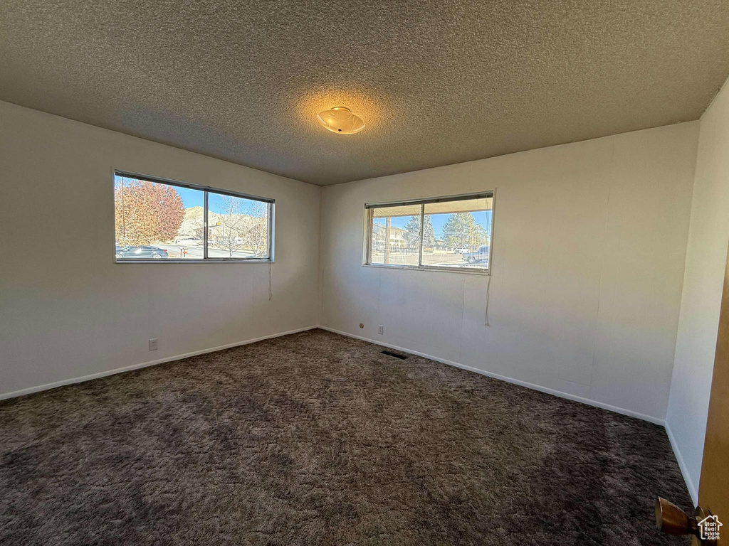 Empty room with dark colored carpet and a textured ceiling