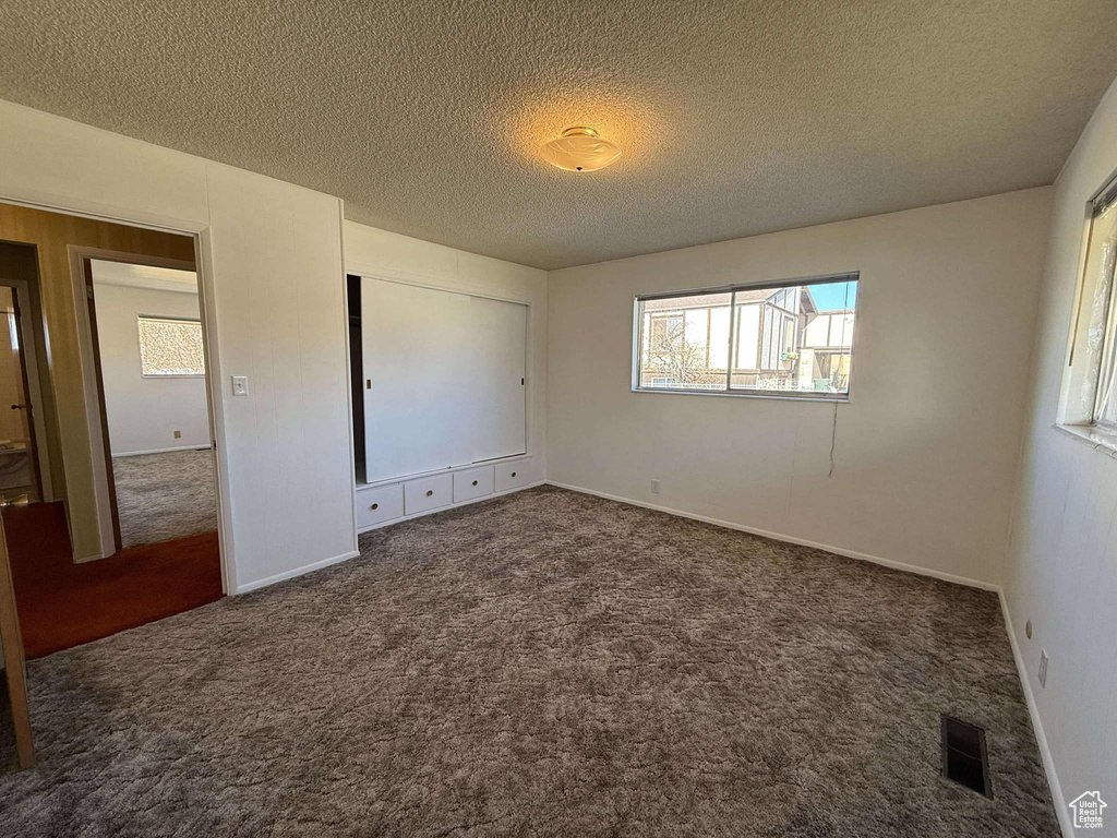 Unfurnished bedroom with dark carpet and a textured ceiling