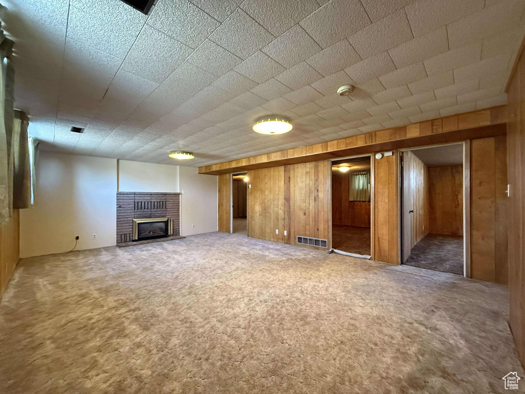 Unfurnished living room with carpet flooring, a brick fireplace, and wooden walls