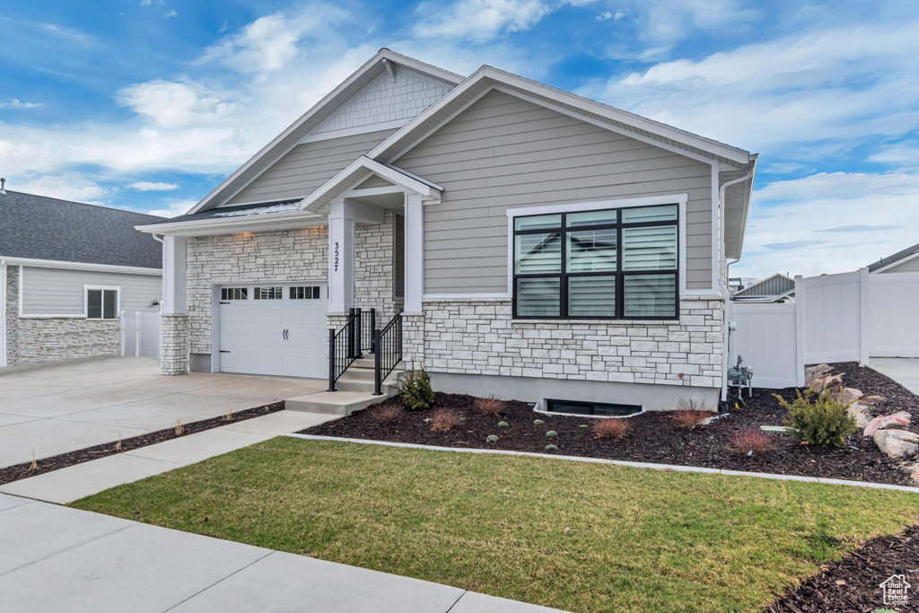Craftsman-style home with driveway, stone siding, a gate, a front yard, and an attached garage