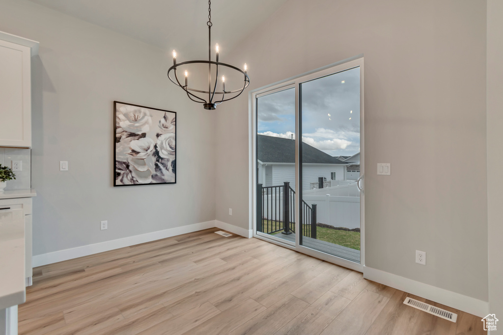 Unfurnished dining area featuring lofted ceiling, visible vents, light wood-style floors, baseboards, and a notable chandelier