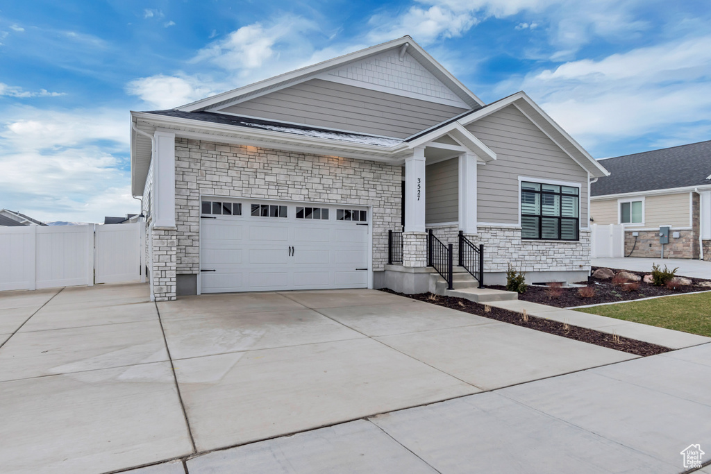 Craftsman-style home featuring fence, driveway, an attached garage, and stone siding