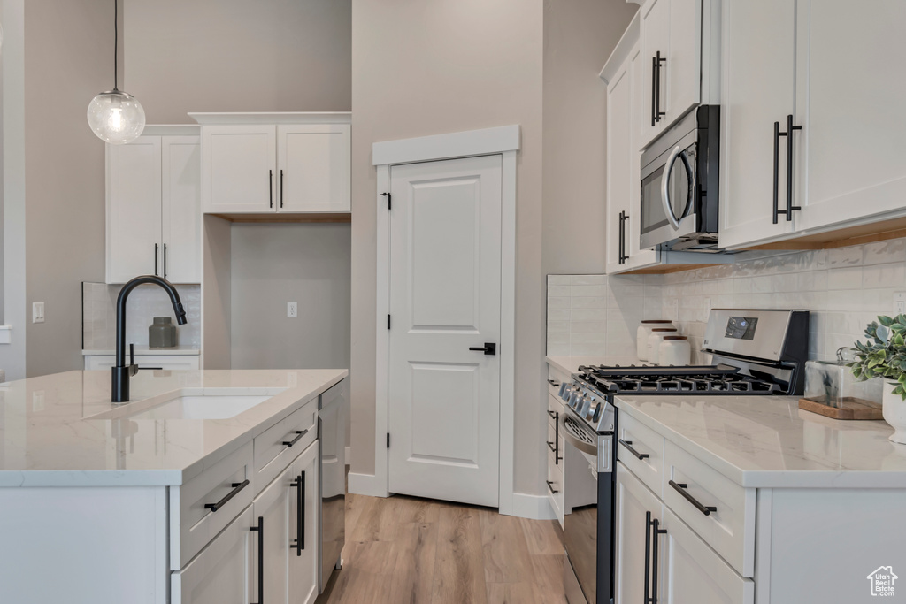 Kitchen with tasteful backsplash, stainless steel appliances, white cabinets, a sink, and light wood-type flooring