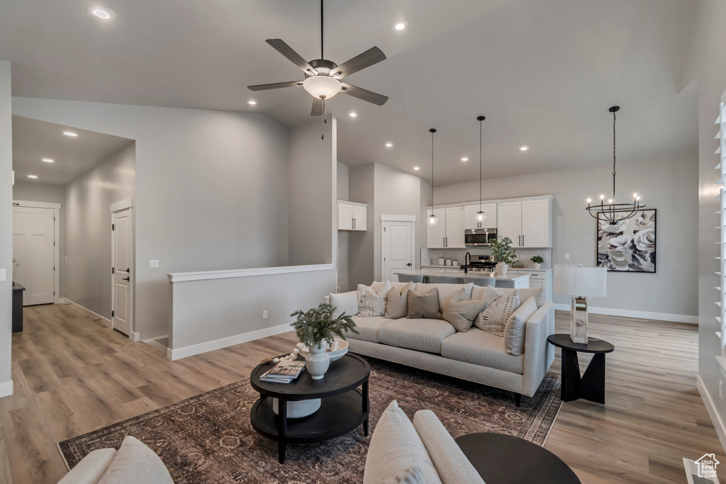 Living area with baseboards, recessed lighting, light wood finished floors, high vaulted ceiling, and ceiling fan with notable chandelier