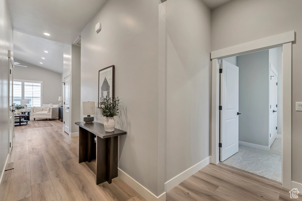 Hallway featuring baseboards, light wood-type flooring, lofted ceiling, and recessed lighting
