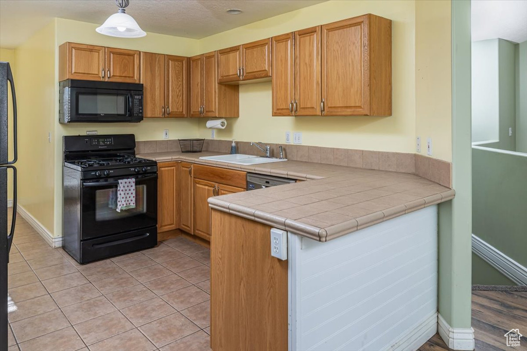 Kitchen featuring tile counters, sink, hanging light fixtures, kitchen peninsula, and black appliances