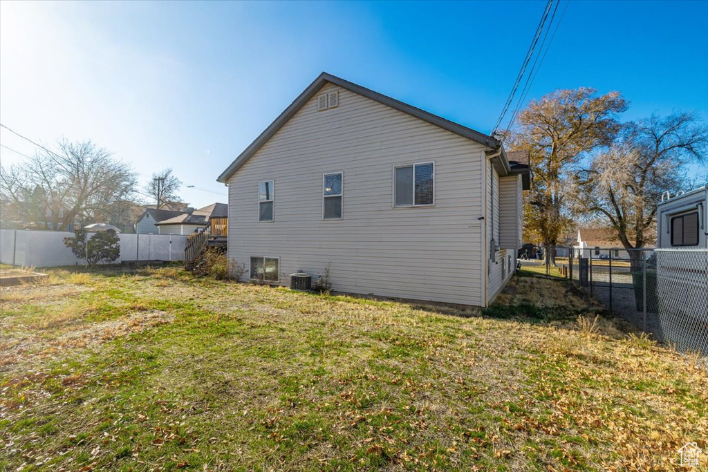 Back of property with central AC unit and a lawn