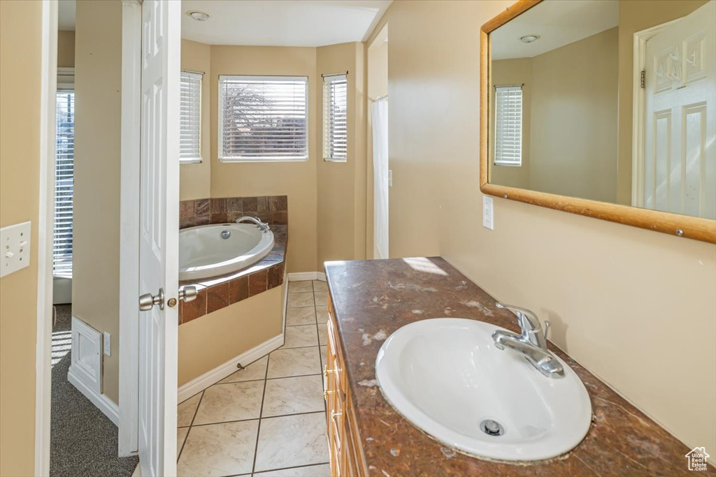 Bathroom with tile patterned floors, tiled tub, and vanity