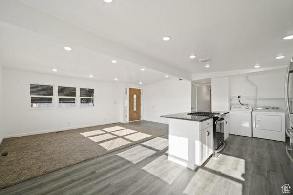 Kitchen featuring stainless steel range with gas cooktop, dark hardwood / wood-style flooring, separate washer and dryer, and white cabinets