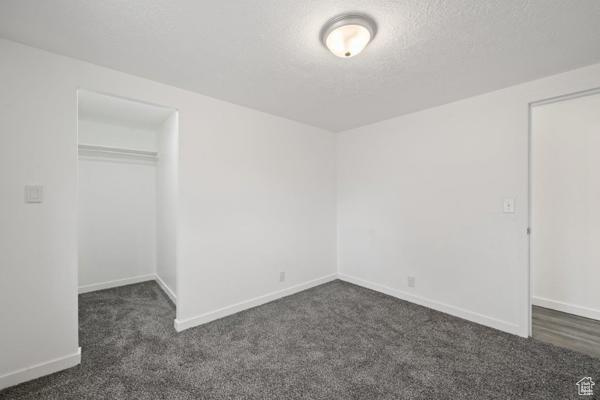 Unfurnished bedroom with a textured ceiling, dark carpet, and a closet