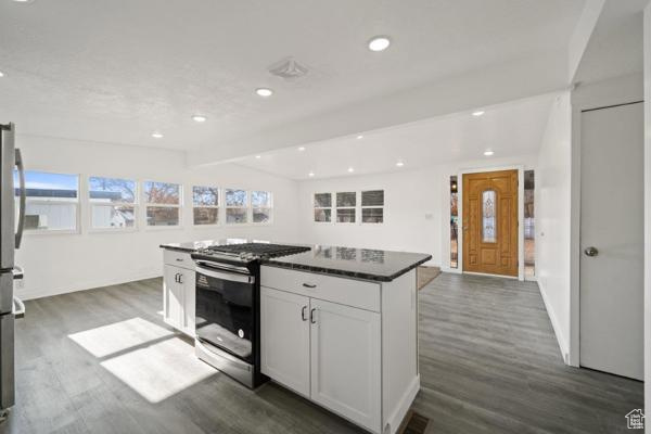Kitchen featuring gas stove, white cabinetry, a center island, and dark wood-type flooring