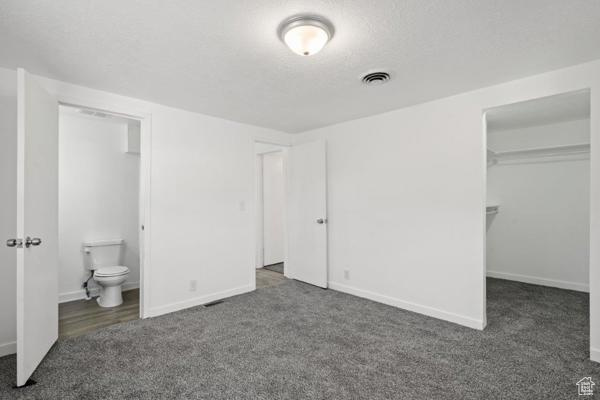 Unfurnished bedroom with ensuite bath, a spacious closet, a closet, and dark colored carpet
