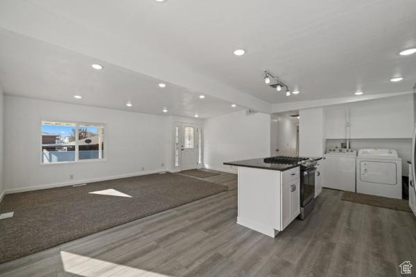 Kitchen with separate washer and dryer, white cabinetry, stainless steel range with gas cooktop, and wood-type flooring