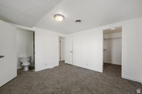 Unfurnished bedroom with ensuite bathroom, dark carpet, a walk in closet, and a closet