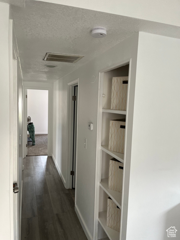 Hallway with a textured ceiling, visible vents, dark wood-style flooring, and baseboards