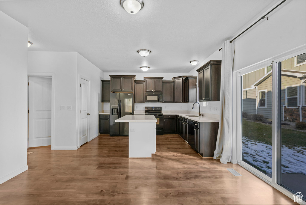 Kitchen with dark hardwood / wood-style flooring, a center island, black appliances, and sink