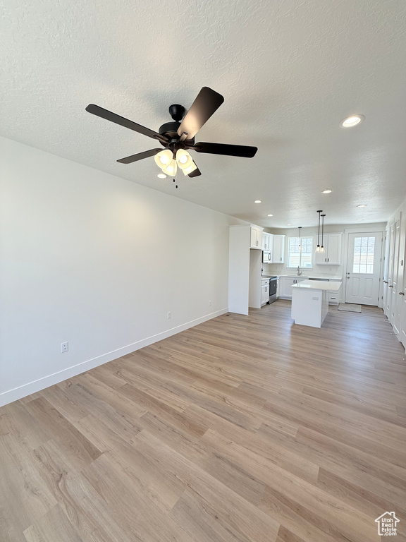 Unfurnished living room featuring light wood-style flooring, recessed lighting, baseboards, ceiling fan, and a textured ceiling
