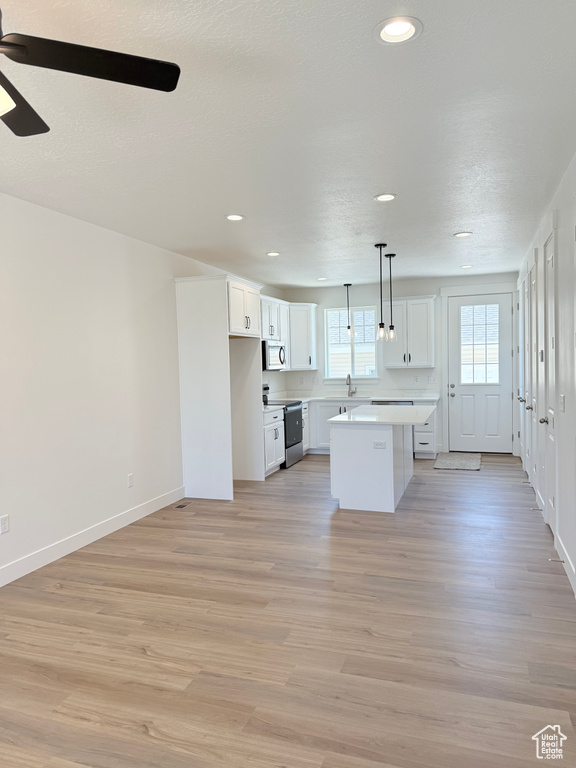 Kitchen with appliances with stainless steel finishes, a ceiling fan, white cabinets, light countertops, and a center island