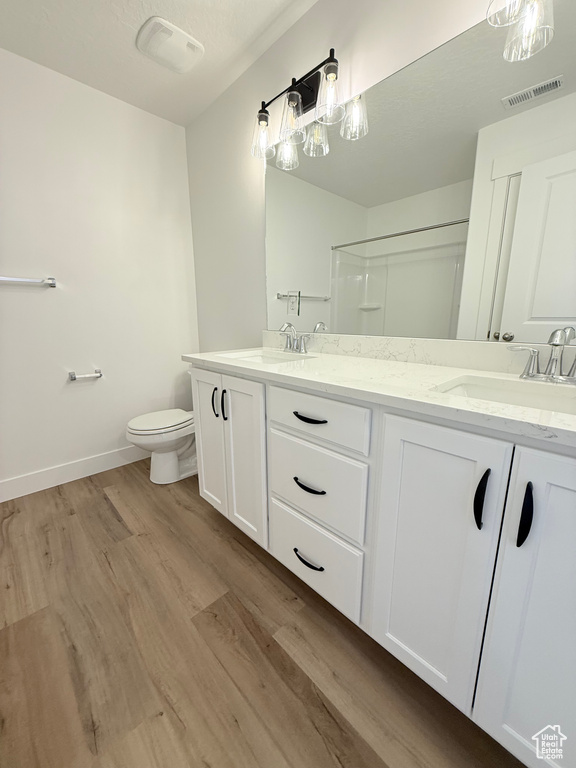 Bathroom with double vanity, wood finished floors, toilet, baseboards, and a shower