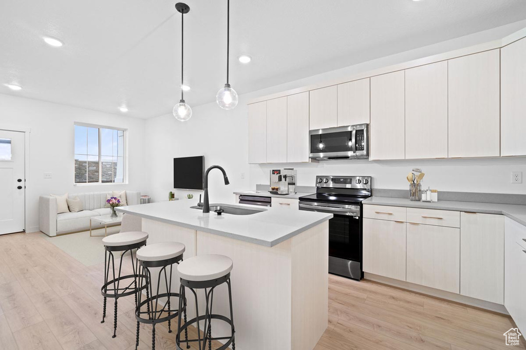 Kitchen with a sink, a kitchen breakfast bar, open floor plan, light wood-style floors, and stainless steel appliances