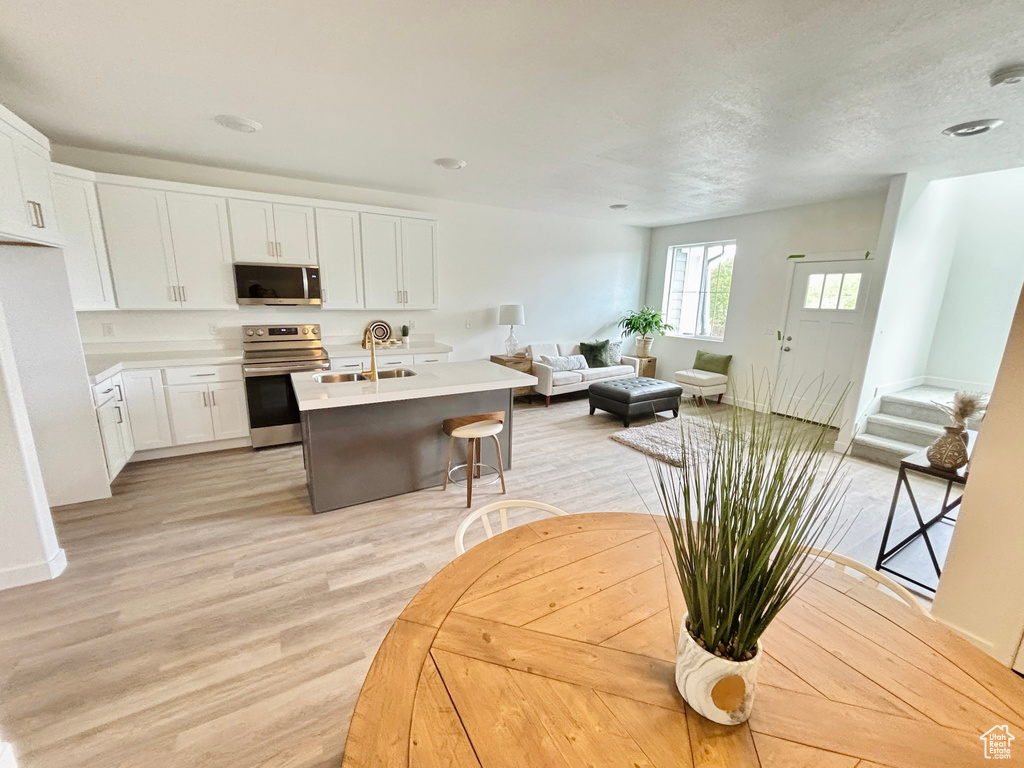 Kitchen with a sink, light wood-type flooring, white cabinetry, open floor plan, and appliances with stainless steel finishes