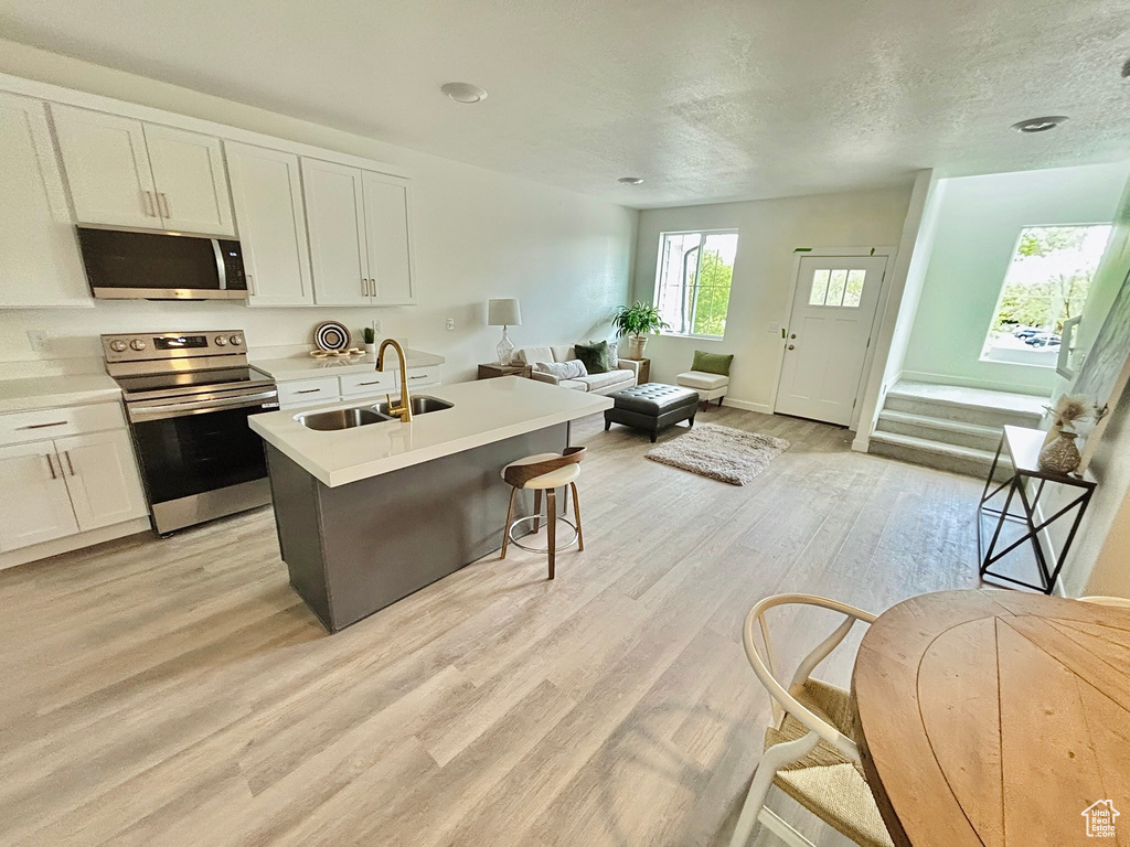 Kitchen featuring a sink, appliances with stainless steel finishes, open floor plan, white cabinets, and light wood-style floors