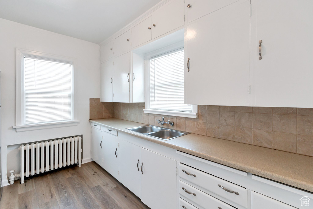 Kitchen with radiator heating unit, white cabinets, light wood-type flooring, and sink