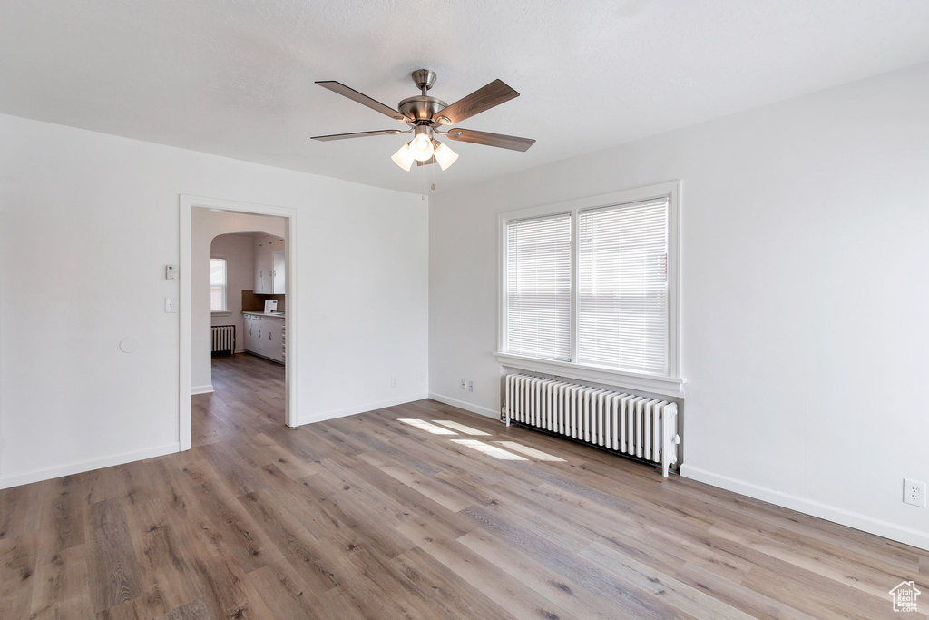 Empty room with ceiling fan, radiator, and light hardwood / wood-style flooring