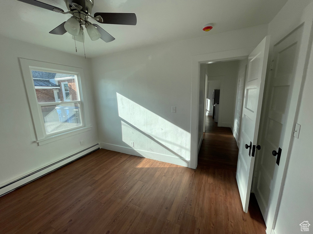 Empty room featuring dark hardwood / wood-style floors, ceiling fan, and baseboard heating