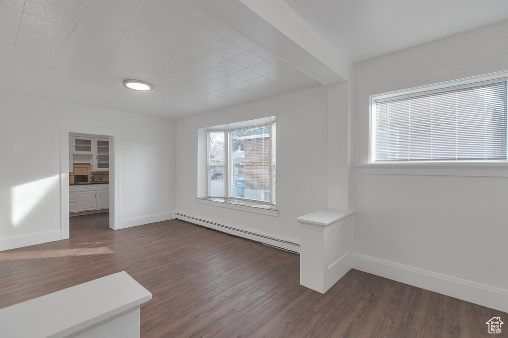 Unfurnished room with plenty of natural light, dark wood-type flooring, and a baseboard heating unit