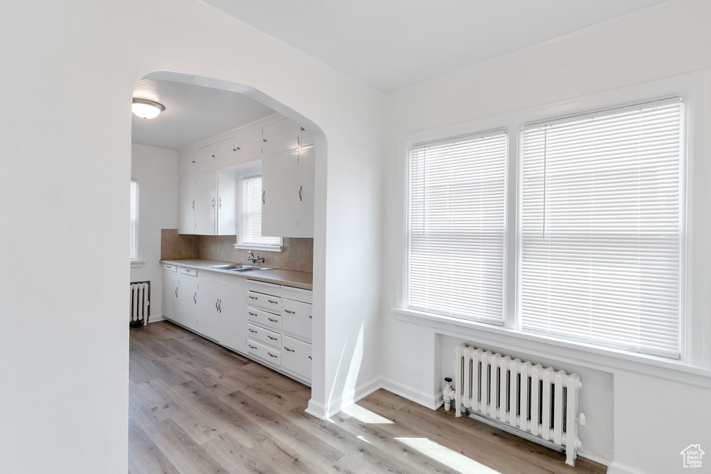 Kitchen featuring radiator, sink, white cabinets, and light hardwood / wood-style floors