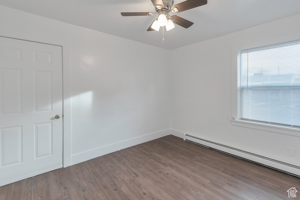 Empty room featuring hardwood / wood-style flooring, ceiling fan, and baseboard heating