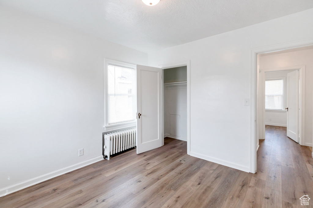 Unfurnished bedroom with multiple windows, a closet, radiator heating unit, and light hardwood / wood-style flooring